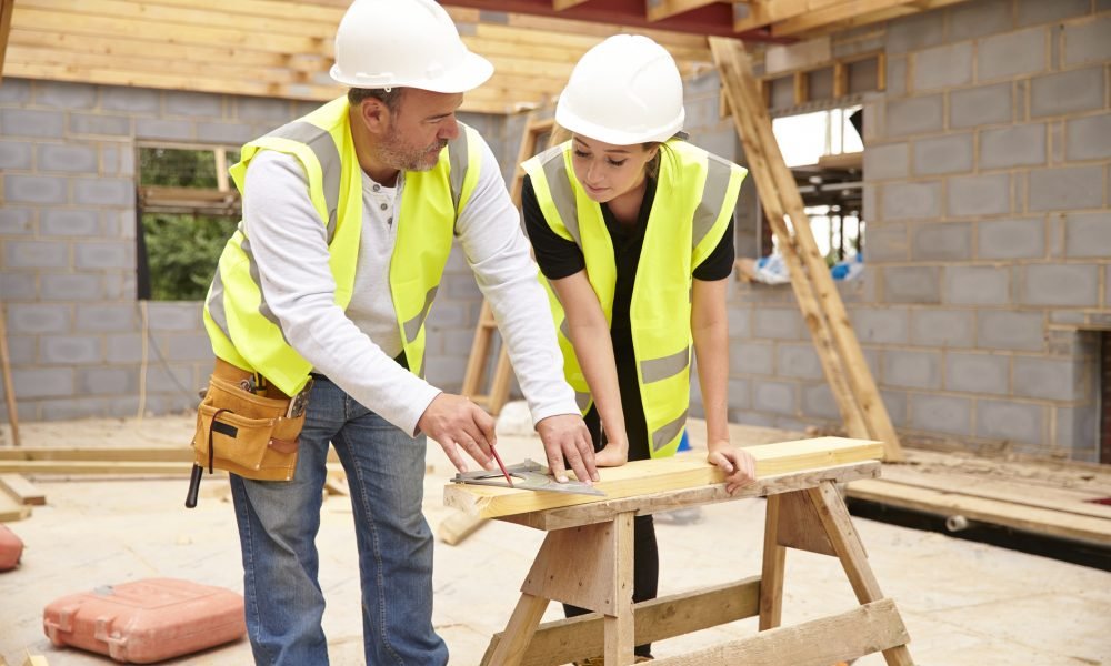 Carpenter With Female Apprentice Working On Building Site