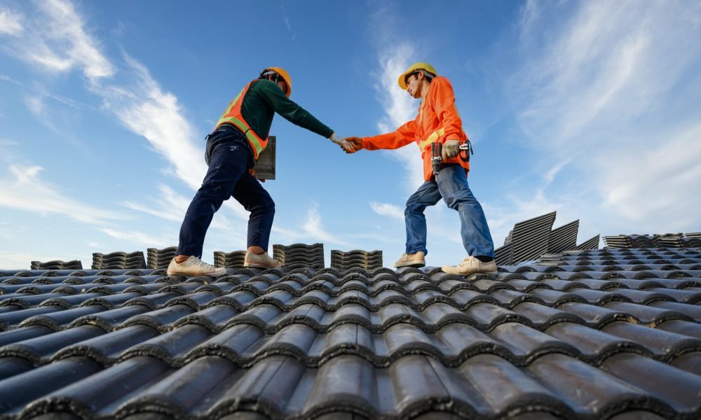 Asian male roof repairman work together as a team standing on the roof Ceramic or cement roof tiles on the construction site